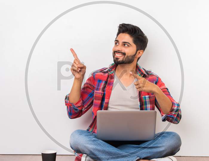 Indian Asian Young Man Using Laptop While Sitting On Floor Presenting Or Pointing At Something