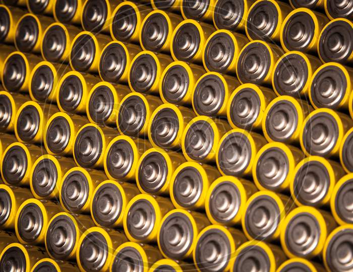 Close View Of Batteries Alkaline 1.5 Volts In Size Aa Several Batteries In Rows.A Close-Up Of The Same Yellow Batteries, Lined Up In Even Rows By Positive Charges. An Unsafe Way To Use Energy.