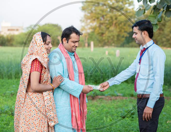 Young Rural Indian Couple Farmer Receive Money From Banker At Agriculture Field.