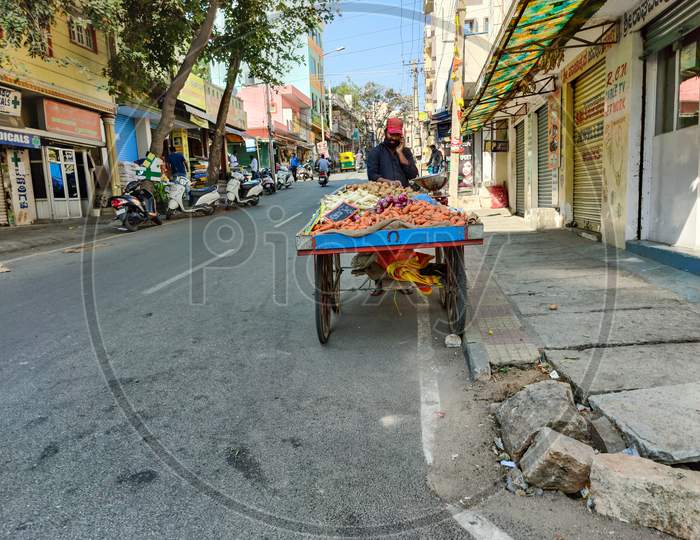 Bangalore, Karnataka , India- February 15Th 2021; Stock Photo Of A Male Vegetable Seller Searing Black Shirt And Red Cap And Speaking On Phone Selling Vegetable On Road At Bangalore City Karnataka India.