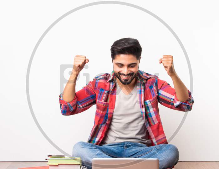 Indian College Students Studying With Laptop And Books Over Wooden Floor Against White Wall