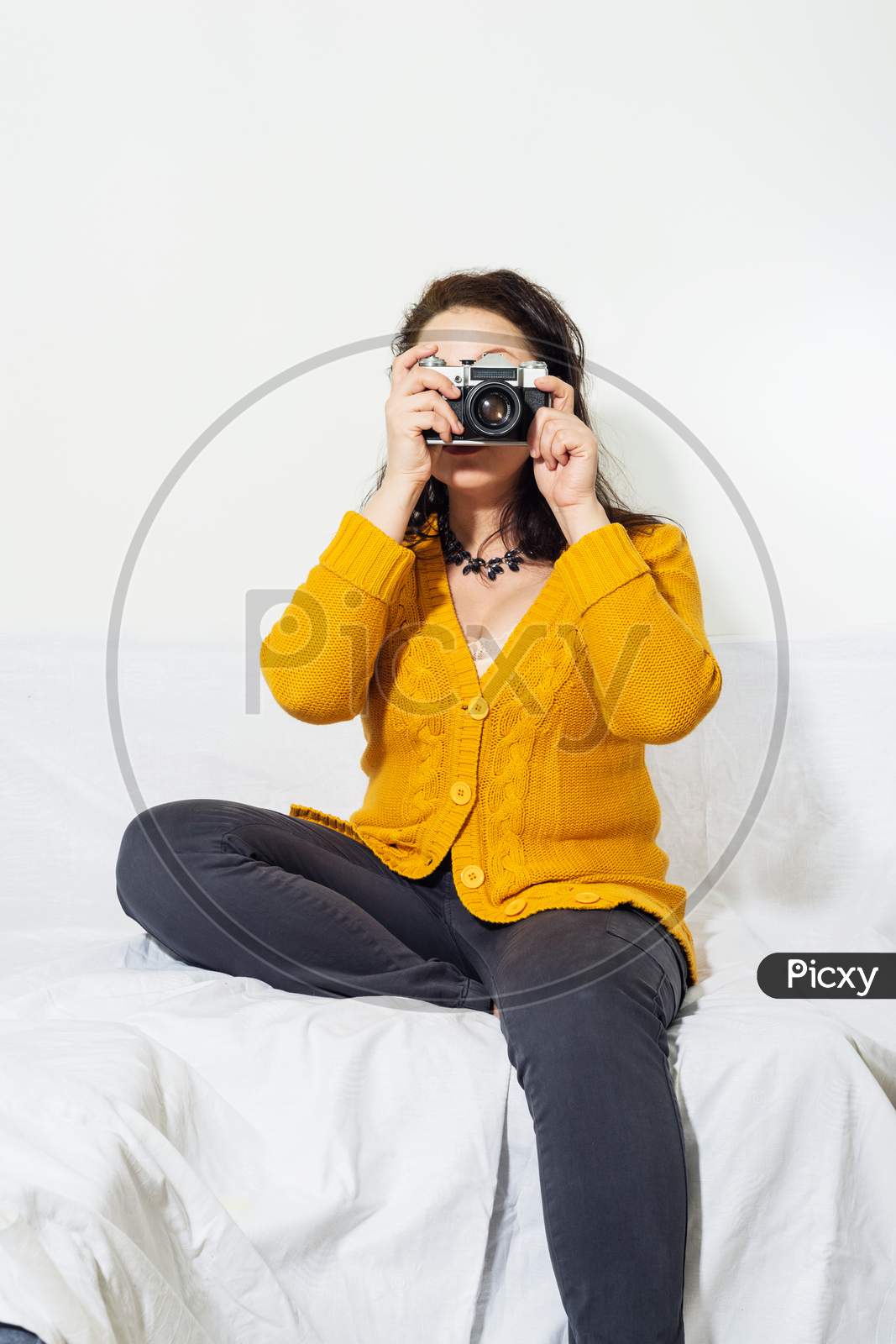 A girl  in buckwheat color knitted sweater photographs with Vintage camera in her hands