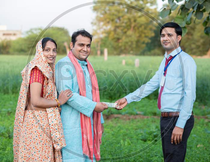 Young Rural Indian Couple Farmer Receive Money From Banker At Agriculture Field.
