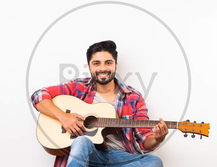 Asian Indian Young Musician Playing Guitar While Sitting Over Wooden Flooring