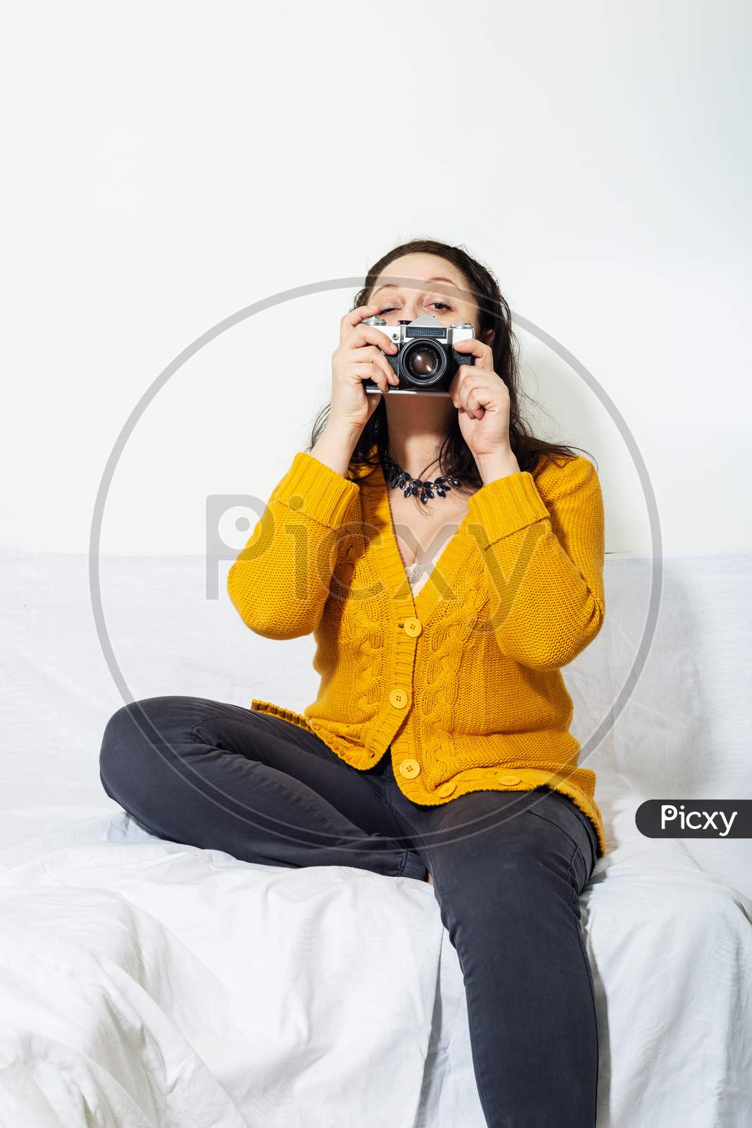 A girl  in buckwheat color knitted sweater photographs with Vintage camera in her hands