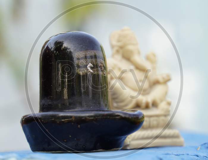 Selective Focus On Black Shivlinga Stature Holding In Sacred Plate With Sacred Bilv Leaves. Prayer Plate Closeup. Hindu Religion And Culture Concept.