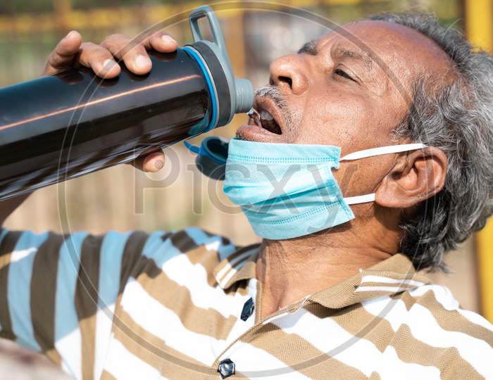 Old Man Drinking Water From Bottle By Placing Mask Below Face During Hot Sunny Day - Concept Of Healthcare, Medical, Thirsty On Outdoors During Coronavirus Or Covid-19 Pandemic.