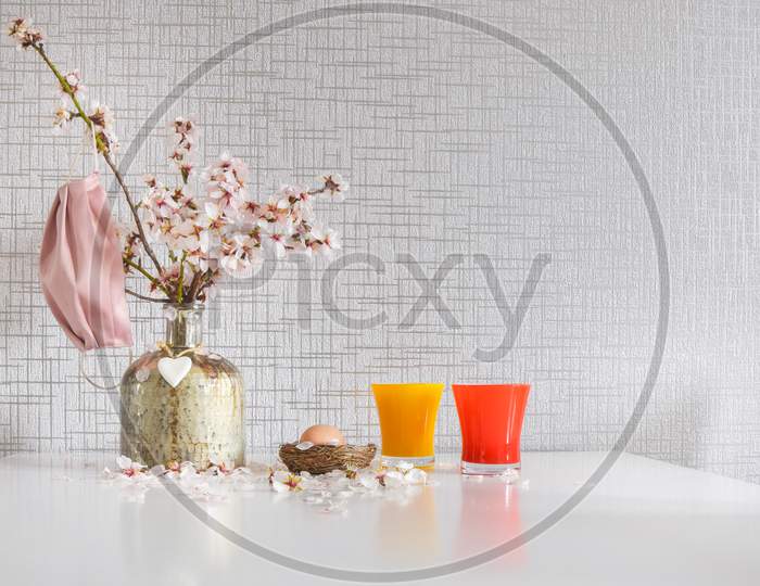Spring Daisy Flowers In Vase With Pink Facial Mask Hanging And Raw Easter Egg On Bright Kitchen Table. Conceptual Safe Easter Anti-Pandemic White Background