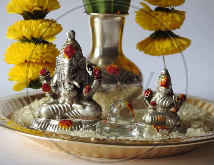 Closeup of silver kalash decorated with chrysanthemum flower, leaf, coconut, kumkum and turmeric with ganesha, lakshmi and shivalinga statue in a plate isolated on white background