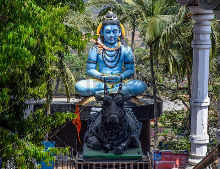 Front View Of Giant Statue Of Lord Shiva And His Vehicle Nandi Bull Under Bright Sunlight Surrounded By Green Trees At Kanheri Math Kolhapur City Maharashtra India. Focus On Statue.