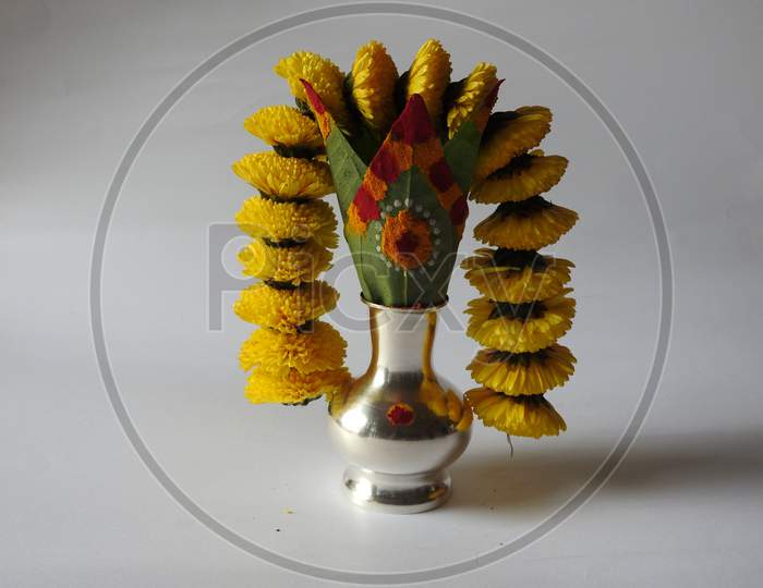 Closeup of silver kalash decorated with chrysanthemum flower, leaf, coconut, kumkum and turmeric with ganesha, lakshmi and shivalinga statue in a plate isolated on white background