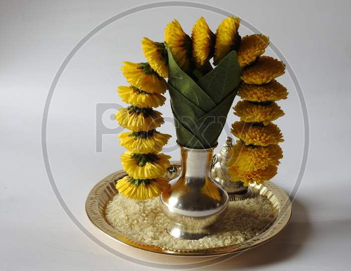 Closeup Of Silver Kalash Decorated With Chrysanthemum Flower, Leaf, Coconut, Kumkum And Turmeric With Ganesha, Lakshmi And Shivalinga Statue In A Plate Isolated On White Background