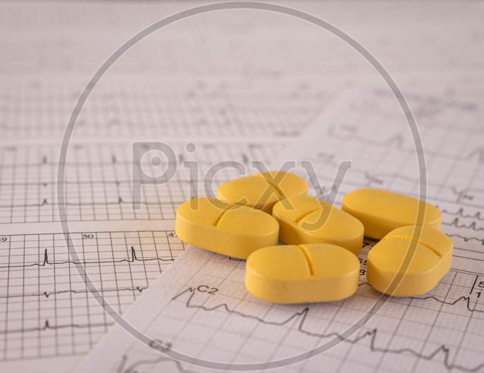 Huge Orange-Yellow Pills On Paper With Ekgs And Cardiac Arrhythmias. Medications For The Heart.