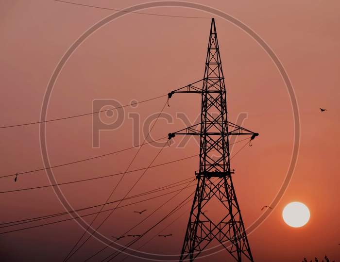 Beautiful Picture Of Big Electricity Tower And Big Orange Sun In Background. Selective Focus On Subject