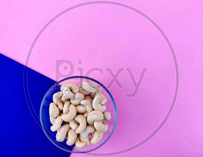 Copy Space Of White Cashew Nuts In Glass Bowl On Blue And Pink Background
