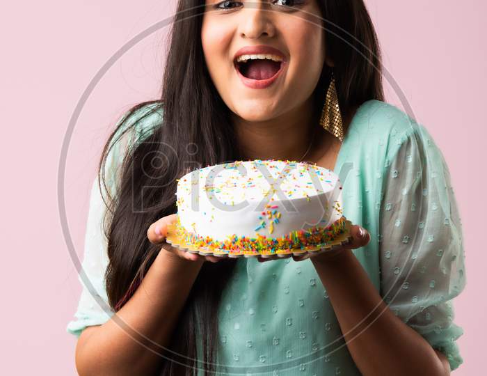 Pretty Indian Asian Woman Holding Decorated Cake Against Pink Studio Background