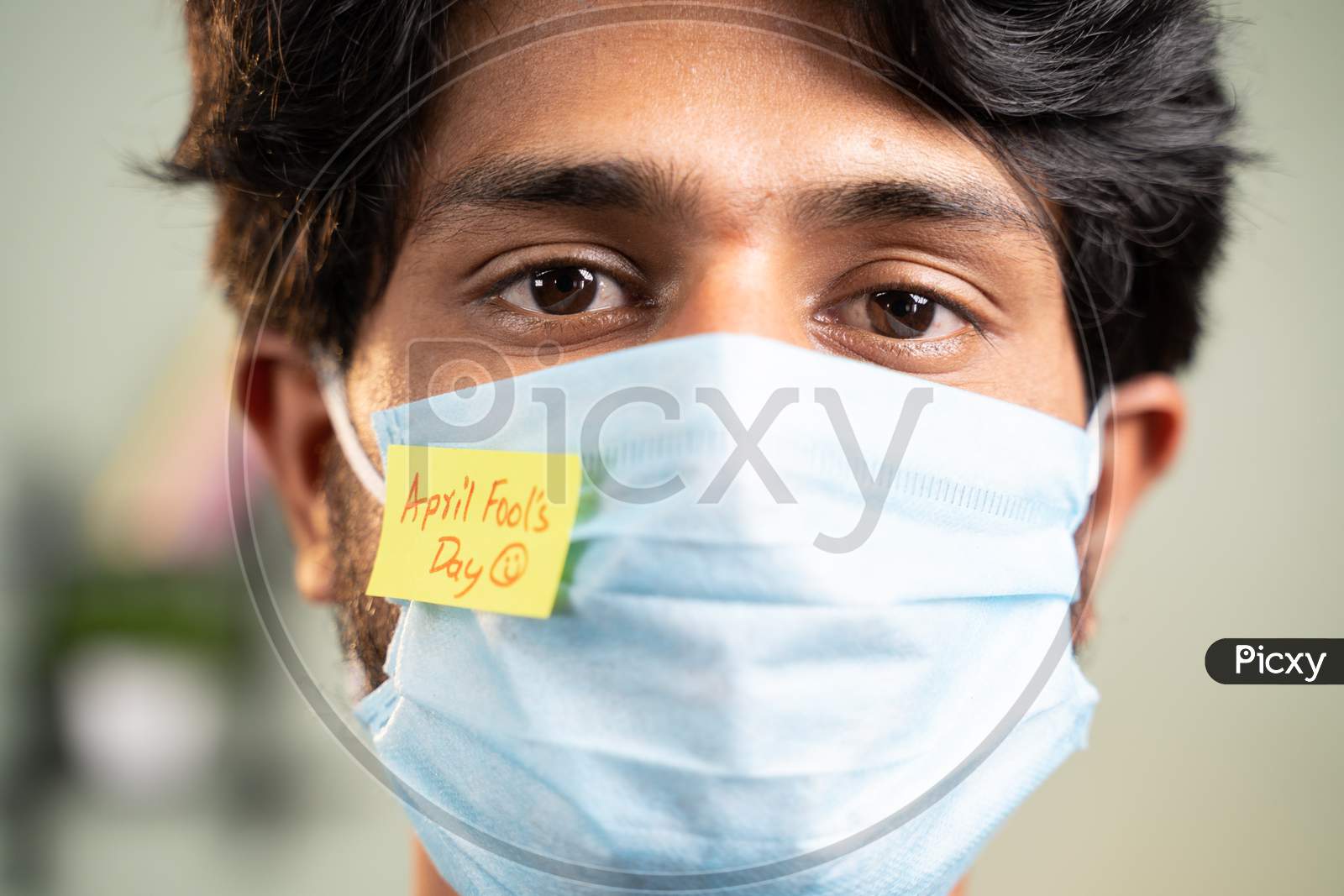 Young Man With Medical Face Mask And April Fools Day Sticker On Mask - Concept Of April Fools Day Celebrations During Coronavirus Covid-19 Pandemic.