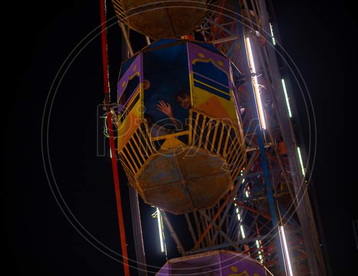 Unidentified Kid Waving From Colourful Giant Wheel At Amusement Park Illuminated At Night In India