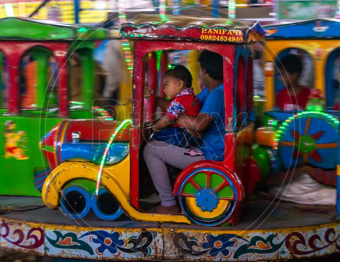 Indian Kid Enjoying Carousel Ride In A Train Engine At Amusement Park