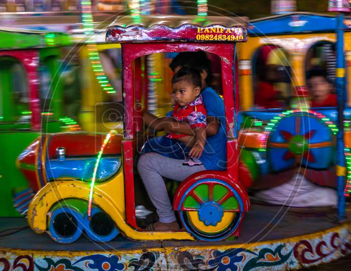 Indian Kid Enjoying Carousel Ride In A Train Engine At Amusement Park