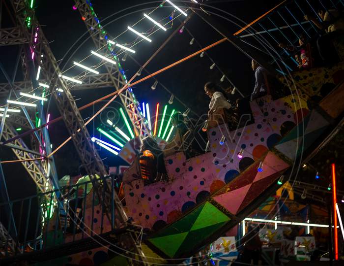 Indian Family Enjoying Thrilling  Ride At Amusement Park Illuminated At Night