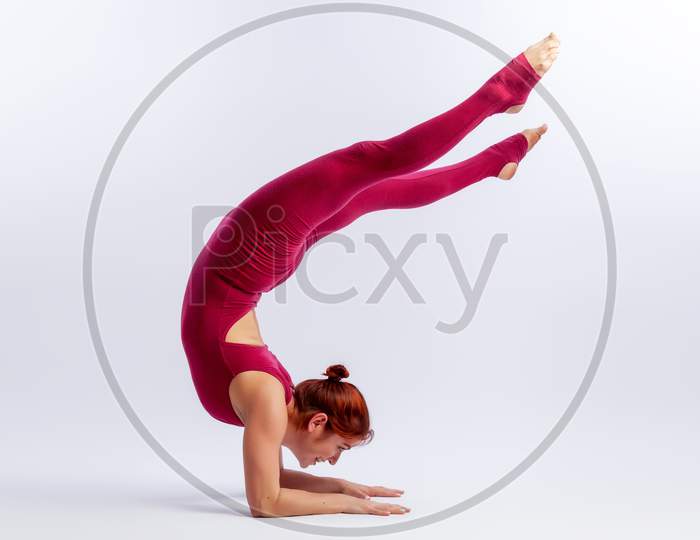 Beautiful Slim Woman In Sports Overalls  Doing Yoga, Standing In An Asana Balancing Pose - Shirshasana  On White  Isolated Background. The Concept Of Sports And Meditation. Training For Stretching And Yoga