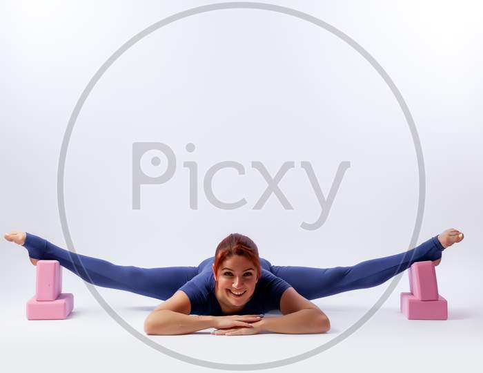 Beautiful Slim Woman In Sports Overalls  Doing Yoga, Standing In An Asana Pose - Twine  On White  Isolated Background. The Concept Of Sports And Meditation. Training For Stretching And Yoga