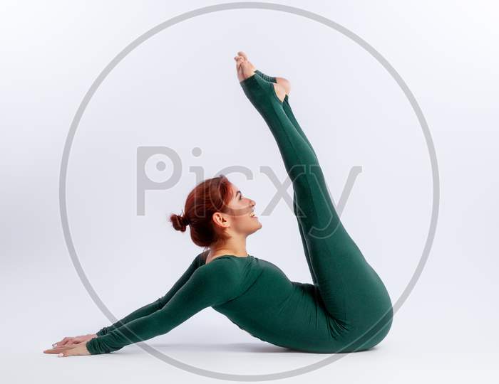 Beautiful Slim Woman In Sports Overalls  Doing Yoga, Standing In An Asana Balancing Pose Ubhaya Padangushthasana  On White  Isolated Background. The Concept Of Sports And Meditation. Training For Stretching And Yoga