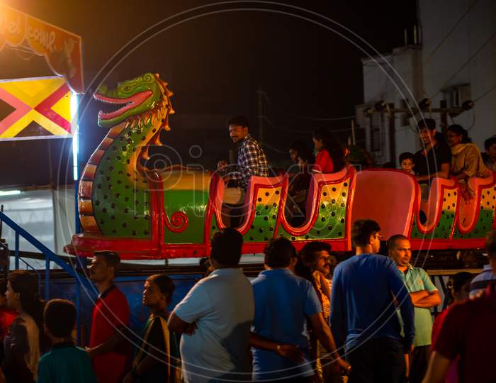 Indian Family Enjoying Thrilling Roller Coaster Ride At Amusement Park Illuminated At Night