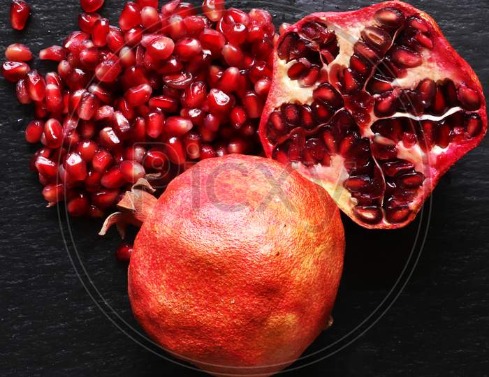 Macro Photography Of Two Organic Pomegranates One Whole And The Other Cut In Half With Its Seeds On Slate Background For Food Illustrations