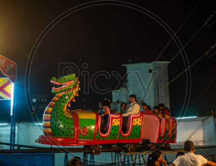 Indian Family Enjoying Thrilling Roller Coaster Ride At Amusement Park Illuminated At Night