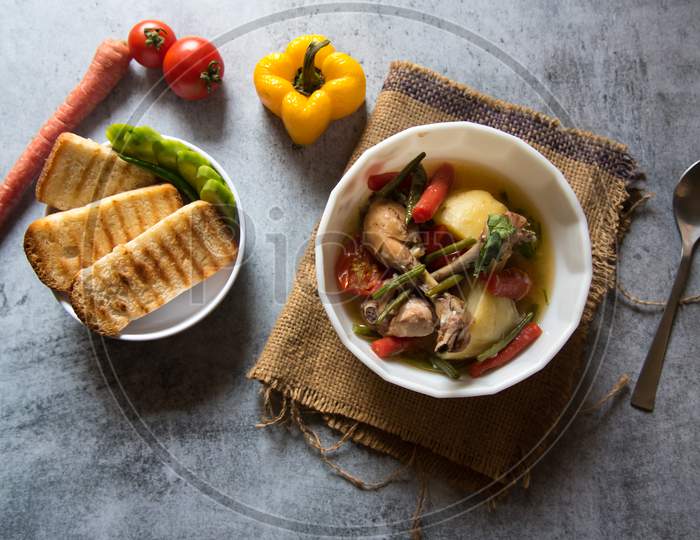 Top view of Chicken stew along with vegetables in a bowl and bread slices