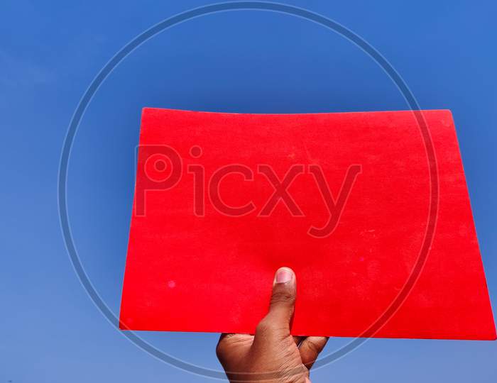 South Indian Man Hand Holding Empty Red Color Sheet Or Paper. Cloud Background.