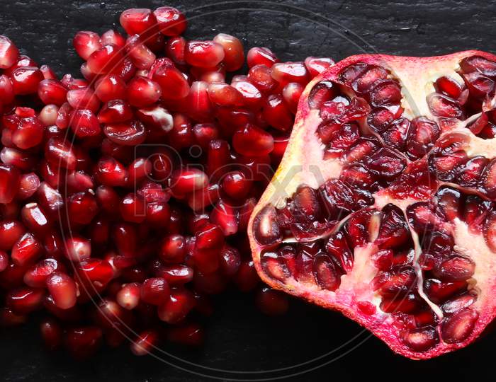 Macro Photography Of An Organic Pomegranate Cut In Half And Of A Handful Of Pomegranate Seeds On Slate Background For Food Illustrations