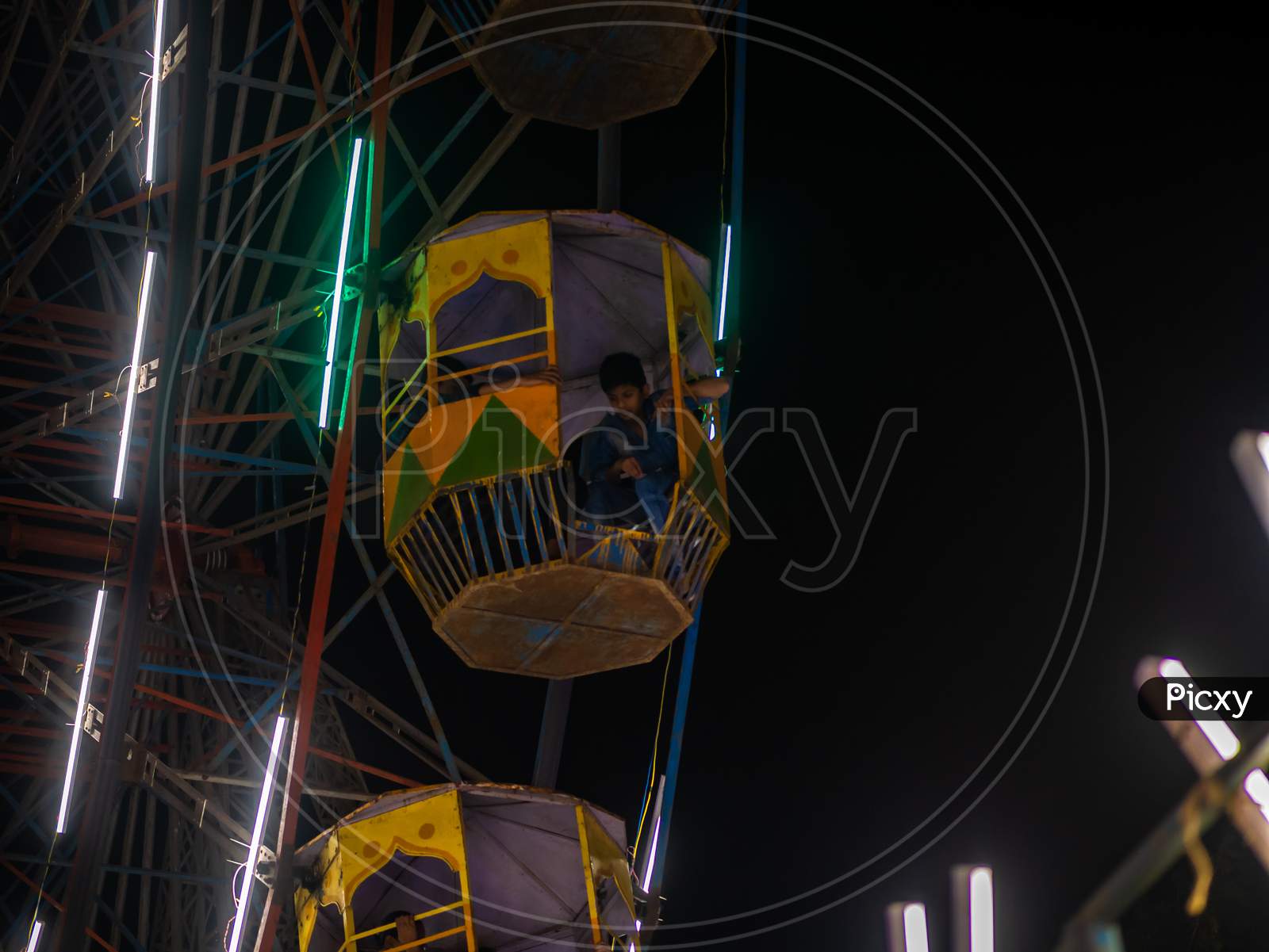 Unidentified Kid Watching From Colourful Giant Wheel At Amusement Park Illuminated At Night In India