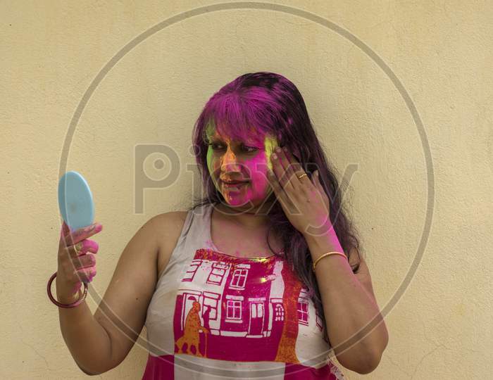 A Young Beautiful Indian Lady Holding A Mirror And Looking At Her Face Full Of Colors.