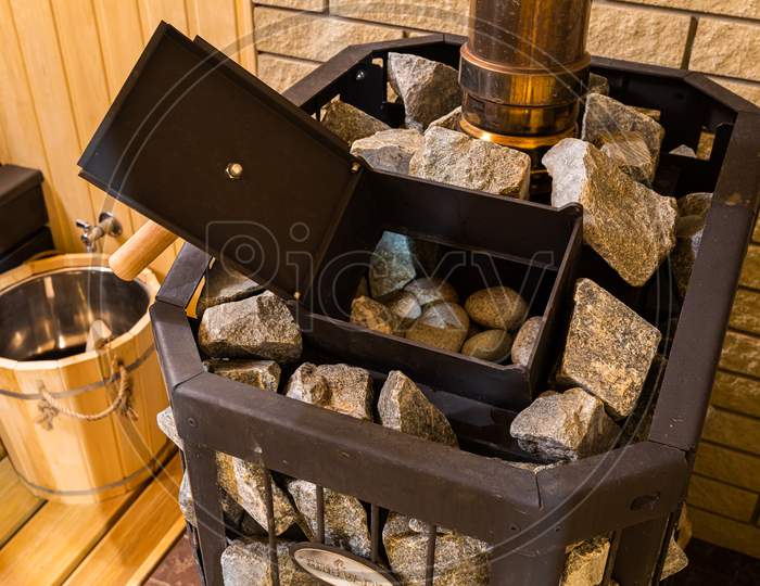 Relax In A Hot Sauna. Hot Stone On Heater In Sauna Spa  Room. Sauna Baked Stove And Wooden Background