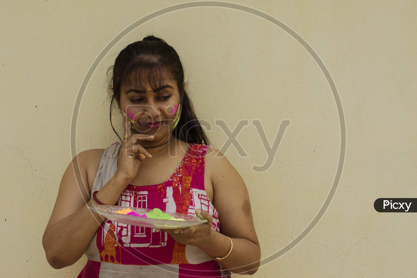 A Young Beautiful Indian Lady Holding A Plate Full Of Holi Colors And Her Face Full Of Colors.
