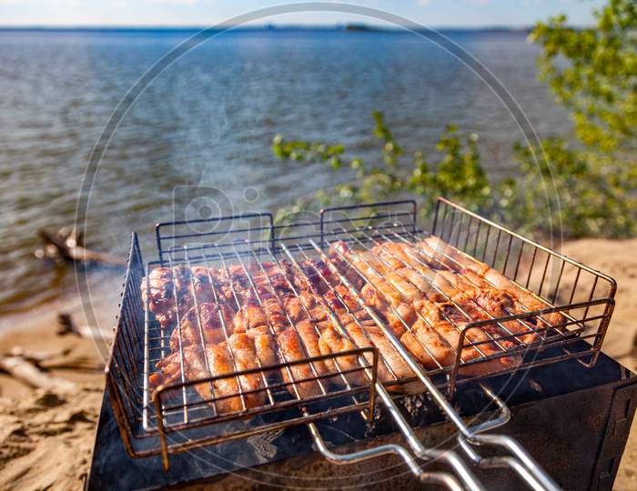 Chiken On The Grill Against The Background Of The Sea And The Beach- Paleo Food Photography.Delicious Chiken Steak, Hot Barbecue Grill.Roasted Chiken Leg Grilled, Bbq. Barbecue, Picnic In Nature