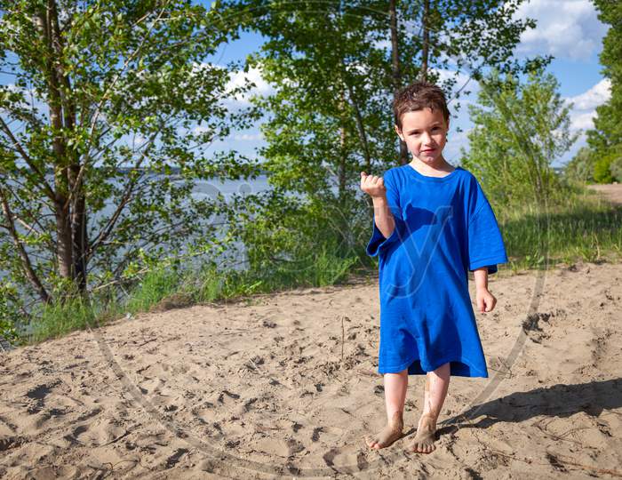 A Little Cheerful Boy In Father'S Fur Coat Is Standing And Basking In The Sun After A Cheerful Swim On A Warm Summer Day On A Sandy Beach. Children'S Holidays And Entertainment