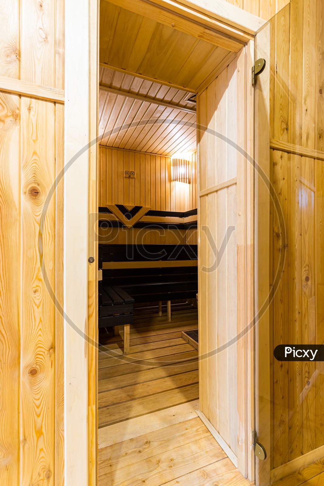A Close-Up Of  Entrance To Wooden Sauna, A Bath With A Large New Metal Stove And Benches With Beautiful Lamps In A Country House