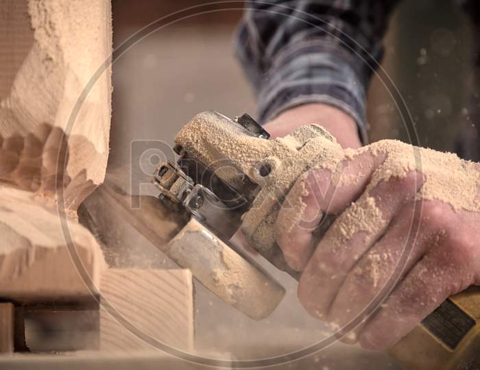 Experienced Carpenter In Work Clothes    Saws A Man'S Head With A Tree , Using An Angle Grinder  In The Workshop, Carpenter'S Hands In Sawdust