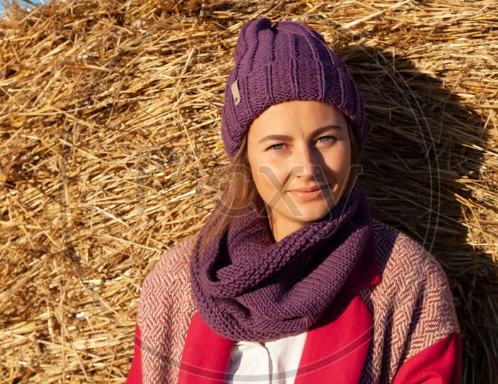 Portrait Of A Beautiful Young Model In Knitted Hat  And Warm Clothes Enjoy Day, On Background Field In  Sunny Autumn Day . Autumn Warm Photo. Woman Smiling And Look Away, Joyful Cheerful Mood.