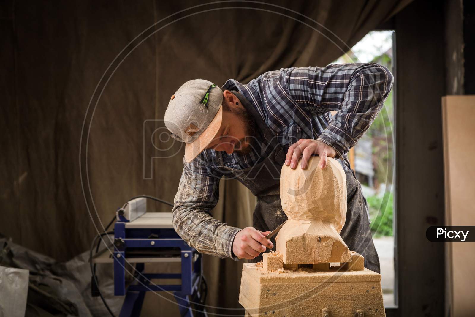 Close Up Of A Carpenter, Builder In Work Clothes Saw To Cut Out Sculpture From Wooden A Man'S Head  In The Workshop, Around A Lot Of Tools,Wooden,Furniture For Work
