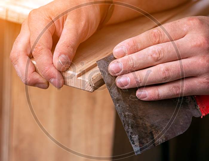 Close-Up A Carpenter In Work Clothes Restoring A Wood With  A Spatula On A Wooden Table. Man Construction Worker Plastering Wooden Block