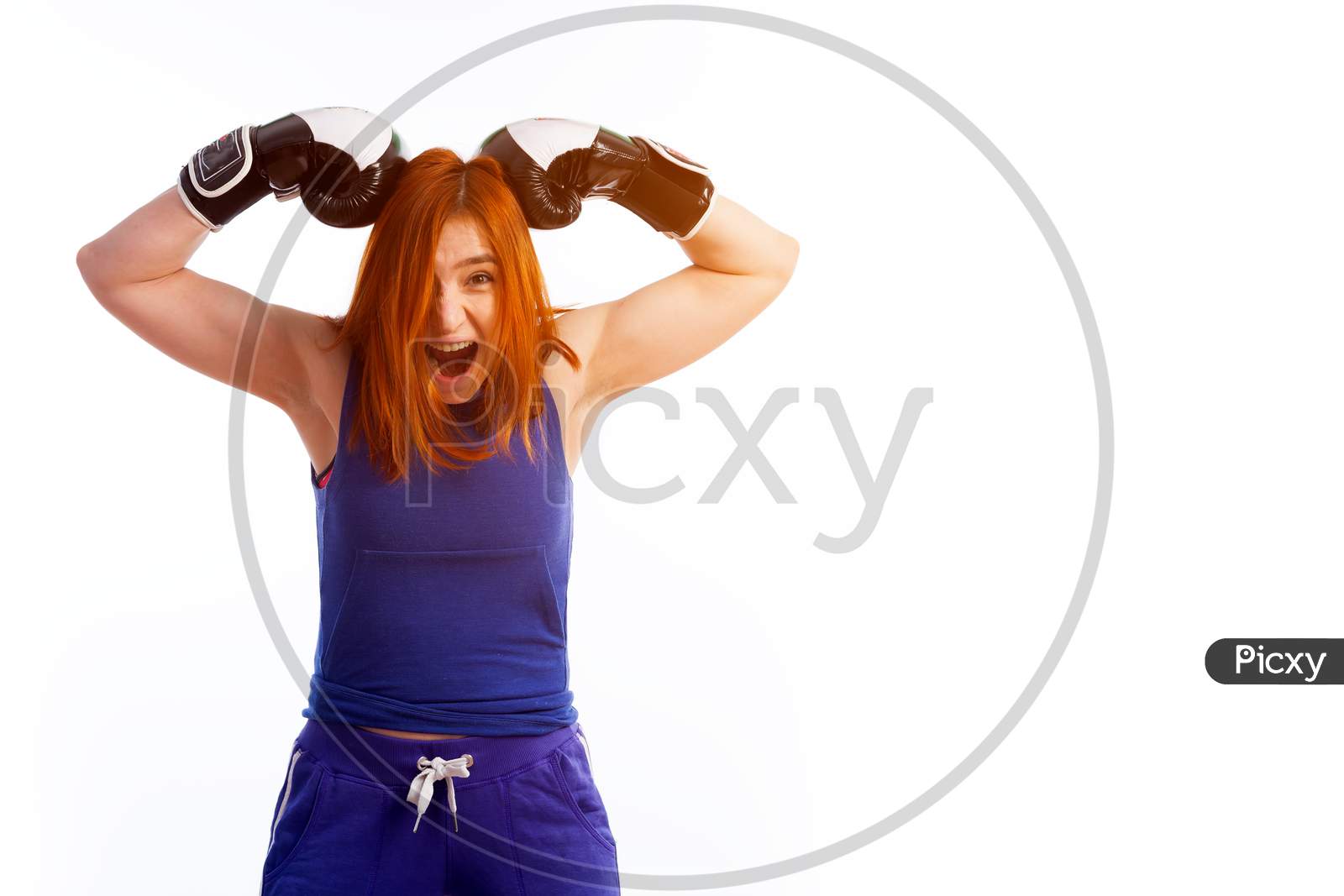 Image of Young Red-Haired Woman In Sportswear And Black And White Boxing  Gloves Smiles And Weakly Strikes Herself With Two Gloves On The Head On A  White Isolated Background-UC274460-Picxy