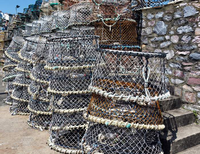 Lobster Pots Stacked Against The Harbour Wall In Brixham