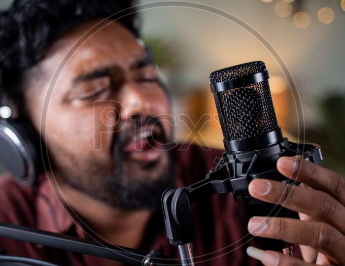 Selective Focus On Microphone, Head Shot Of Young Man With Headphones Singing In Studio - Concept Of Vlogger Or Content Creataor Podcasting