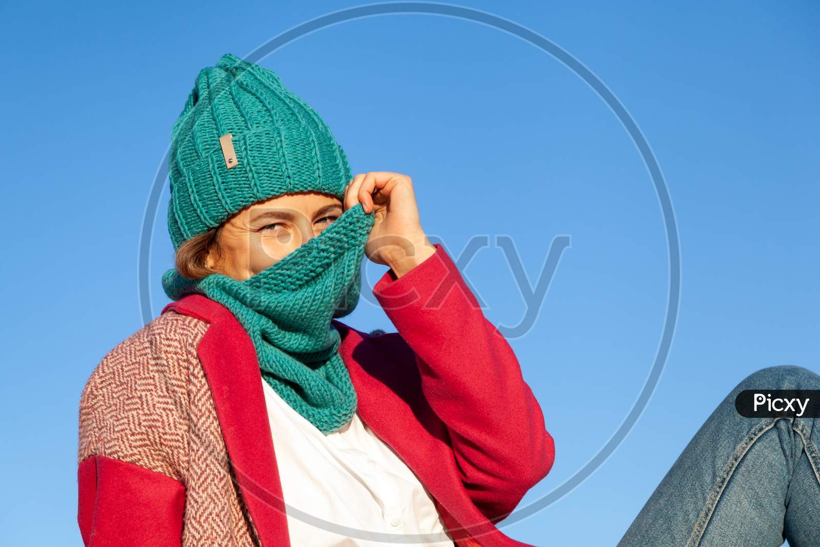 Portrait Of A Beautiful Young Model In Knitted Hat  And Warm Clothes Mysteriously Holds A Scarf Like A Veil, Enjoy Day,Around Blue Sky In  Sunny Autumn Day . Autumn Warm Photo. Woman Smiling And Look At The Camera, Joyful Cheerful Mood.