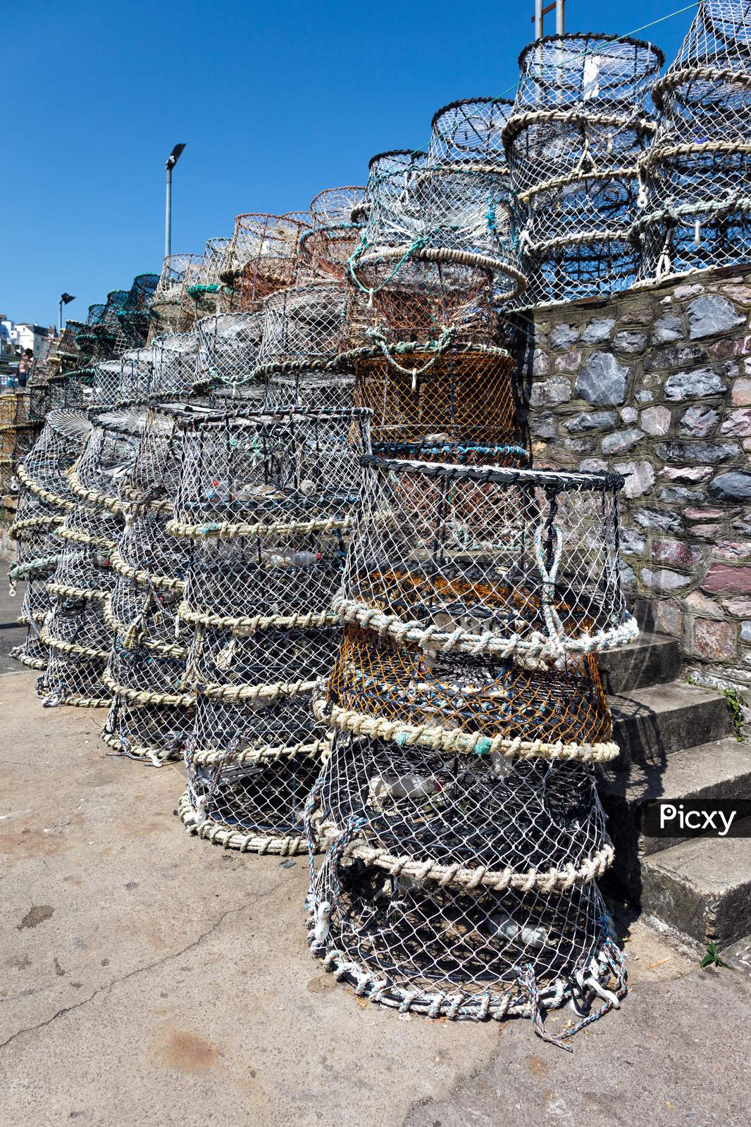 Lobster Pots Stacked Against The Harbour Wall In Brixham